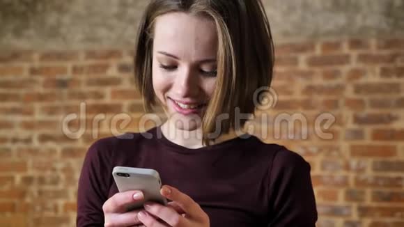 年轻可爱的女孩正在她的智能手机上阅读信息她感到惊讶沟通观念砖背景视频的预览图