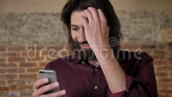 年轻有魅力的黑发男子蓄着胡须正在看着智能手机拨发砖背景交流视频的预览图