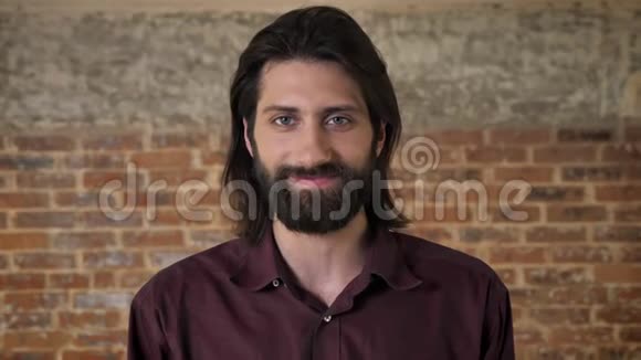 年轻漂亮的黑发男人留着胡子在镜头前看着咯咯地笑着背景是砖视频的预览图