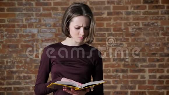 年轻认真的漂亮女孩正在看书微笑着砖背景视频的预览图