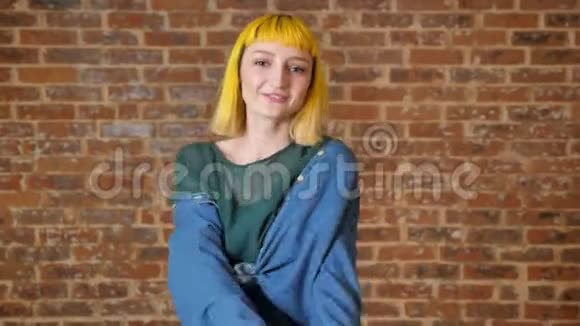 年轻的不寻常的女人有着黄色的头发跳舞看着摄像机被隔离在砖墙的背景上视频的预览图