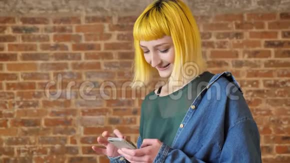 年轻的不寻常的少年黄毛站立在砖墙背景附近打电话发短信微笑积极视频的预览图