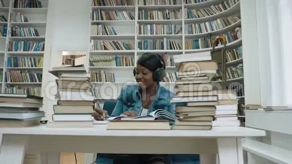 快乐的非洲年轻女子在为大学写讲座时在耳机里听音乐视频的预览图