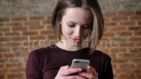 年轻漂亮的女孩正在智能手机上阅读信息笑交流理念砖背景视频的预览图