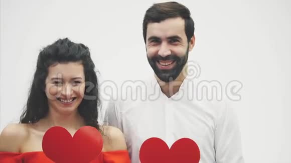 一对美丽的浪漫夫妇被隔离在白色背景下漂亮的年轻女子和英俊的男子抱着红心视频的预览图