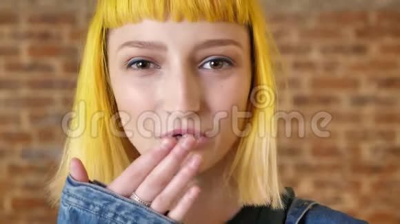 年轻美丽的女人的肖像黄色的头发在镜头前给予空气亲吻微笑快乐砖墙背景视频的预览图