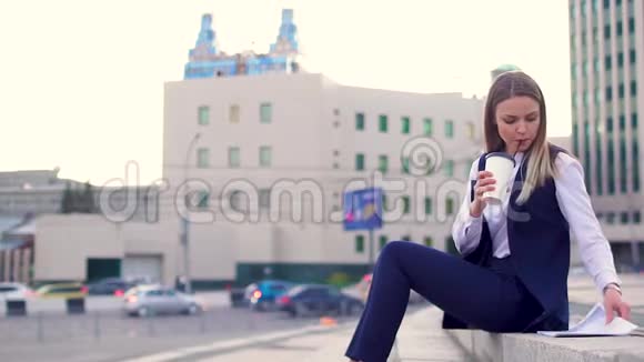 一个穿着办公室西装的年轻女孩坐在楼梯上学习报纸喝咖啡视频的预览图