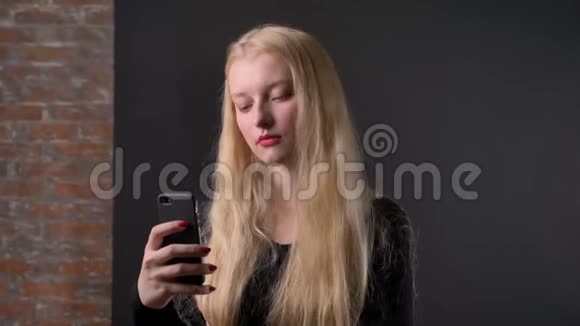 年轻可爱的金发女孩涂着粉红色口红正在智能手机上输入信息交流概念gery背景视频的预览图