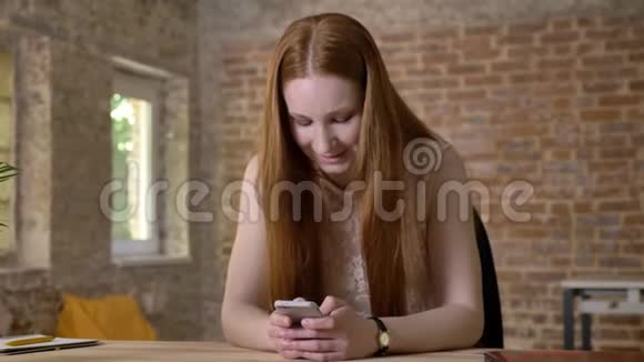年轻的生姜女孩正在她的智能手机上输入信息在相机上观看交流理念砖背景视频的预览图