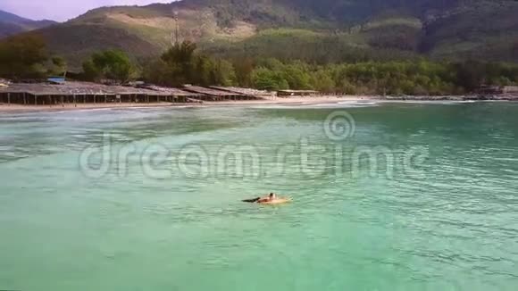女人躺在沙滩上的冲浪板上划着波浪视频的预览图