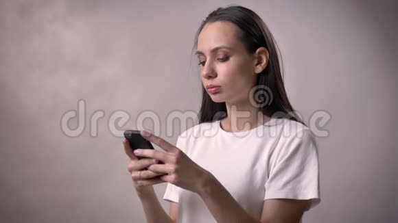 年轻严肃的黑发女孩正在智能手机上输入信息交流概念灰色背景视频的预览图