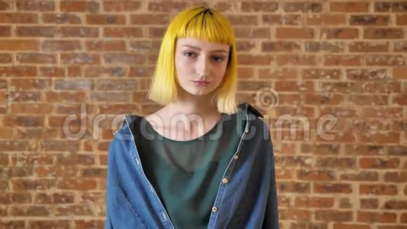 年轻漂亮的女人一头黄发看着摄像机站在砖墙的背景附近不寻常的人视频的预览图