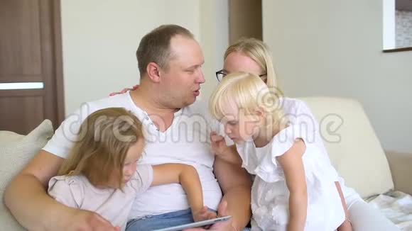 快乐的家庭一起玩笔记本电脑和数字平板电脑在家里爸爸妈妈和两个孩子坐在沙发上视频的预览图