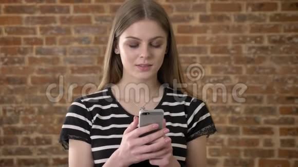 年轻可爱的金发女郎正在智能手机上输入信息思维概念沟通概念砖背景视频的预览图