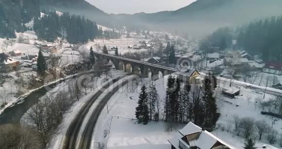 一辆汽车在一个白雪覆盖的村庄4K超高清的铁路桥下通过的鸟瞰图视频的预览图