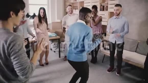 开朗的非裔美国人经理与同事在有趣的休闲办公室庆祝聚会慢动作的圆圈跳舞视频的预览图