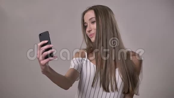 年轻迷人的害羞女孩正在智能手机上自拍玩头发微笑交流理念灰色视频的预览图