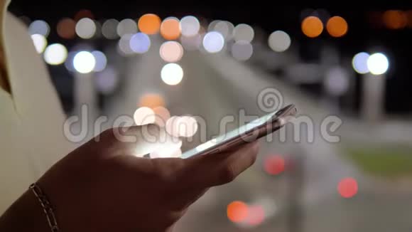 晚上在街道模糊的灯光下用智能手机闭上双手视频的预览图