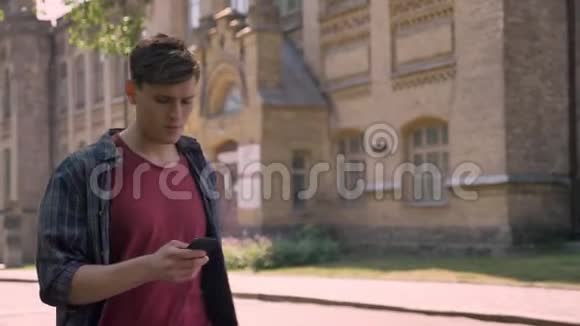 年轻的帅哥在夏天的白天走在大街上敲着智能手机打电话交流视频的预览图