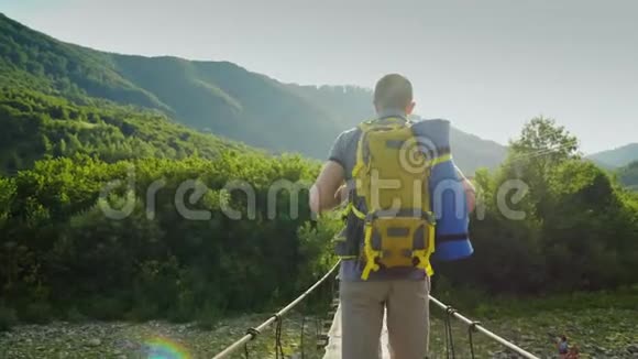 一个背着背包的旅行者沿着一座摇摇晃晃的桥在一条山河上行走背面视频的预览图