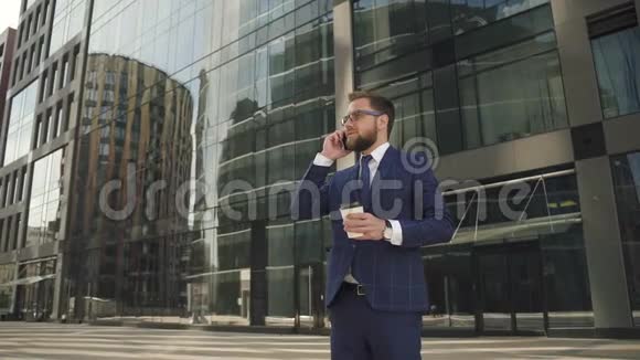 成功的商人穿着蓝色西装拿着咖啡杯在外面打电话视频的预览图