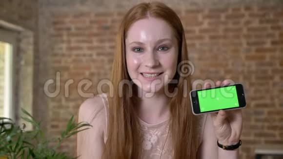 年轻的生姜女孩在智能手机上显示绿色屏幕在镜头下观看交流理念砖块视频的预览图