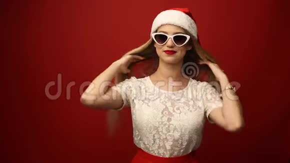 戴着圣诞老人帽子戴着墨镜的迷人金发女郎红色的背景特写肖像视频的预览图