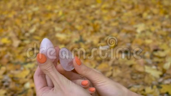 女性双手用橙色指甲手里拿着两个由粉红色石英和透明紫紫水晶制成的蛋黄蛋视频的预览图