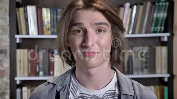 戴着鼻环的年轻长发男子正在镜头前观看表示接受背景是图书馆视频的预览图