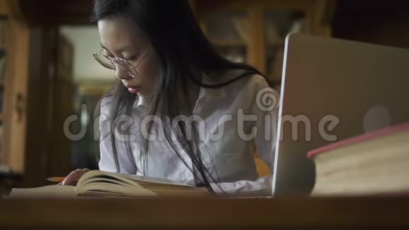 漂亮的学生学习主题坐在桌子上图书馆里有书和笔记本电脑视频的预览图
