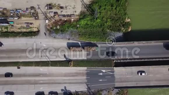 穿越绿色彩色河流跨桥的木材卡车的鸟瞰图飞行在原木炮台上的电影镜头视频的预览图