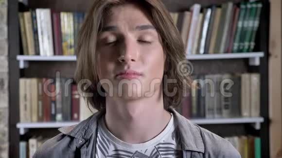 年轻的留着鼻环的长发男子正在镜头前观看整理头发图书馆里模糊的背景视频的预览图