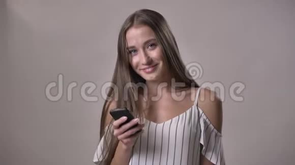 年轻迷人的女孩拿着智能手机看着摄像机微笑着交流理念灰色背景视频的预览图