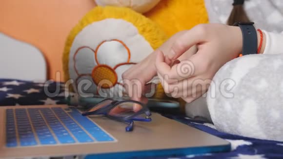 少女穿着温暖的睡衣躺在床上通过笔记本电脑上的互联网手的特写视频的预览图