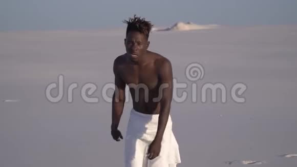 一个精疲力竭的黑人穿着白色的紧身衣缓慢地走在沙漠中视频的预览图