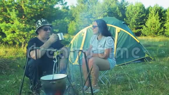 男人和女人的游客坐在帐篷里喝着茶看着锅挂在火上视频的预览图
