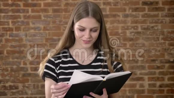 年轻可爱的金发女郎正在看书拇指覆盖页微笑砖背景视频的预览图