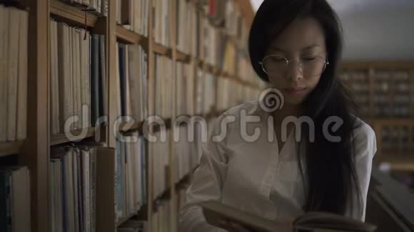 戴圆杯眼镜的年轻亚洲女人把书放在书架上视频的预览图