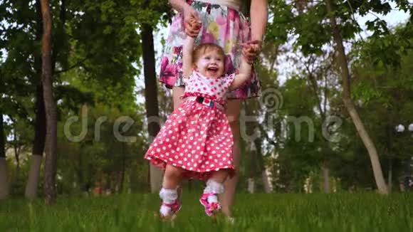 婴儿在空气中旋转在她妈妈的怀里笑女孩很高兴和她的父母在城市公园的绿草上玩视频的预览图