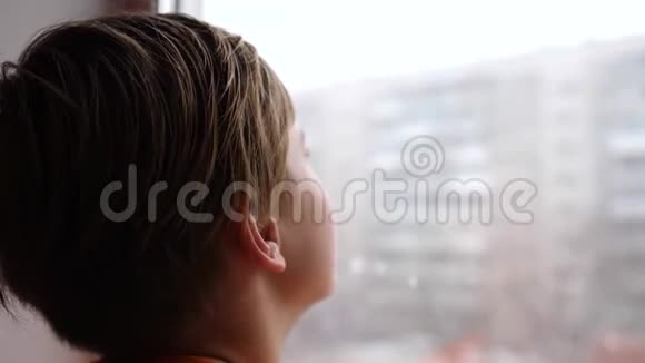 阳光明媚的冬天白天一个年轻人站在窗户旁边看着飘落的雪视频的预览图
