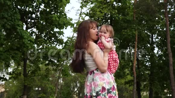 妈妈把婴儿抱在怀里亲吻他的脸颊女孩在绿色公园和她的父母笑慢动作视频的预览图