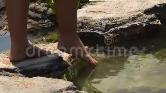女人用脚趾头蘸水来测试雨林中的岩石河的温度年轻女孩在测试水视频的预览图