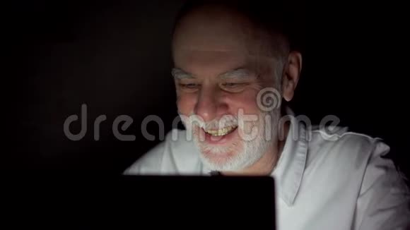 一位老人在夜间通过笔记本电脑上的信使应用程序进行视频聊天只有一张漆黑的脸视频的预览图