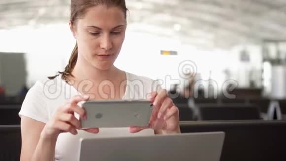 女人在机场候机室用笔记本电脑工作商务旅行中的临时女商人使用智能手机视频的预览图