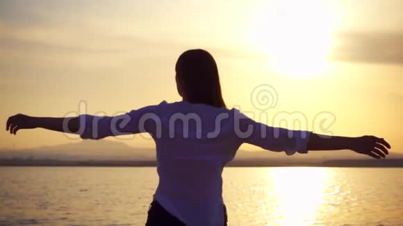 年轻女子在湖上日落时旋转的剪影女性在黄金时间慢动作舞蹈视频的预览图