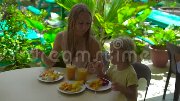一位年轻女子和她儿子在热带花园吃水果晚餐时的慢镜头视频的预览图