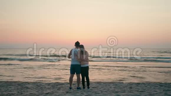 爱的情侣拥抱看着夏日夕阳下的海水浪潮视频的预览图