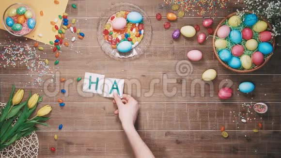 人们把复活节快乐这个词放在用复活节彩蛋装饰的桌子上顶部视图视频的预览图
