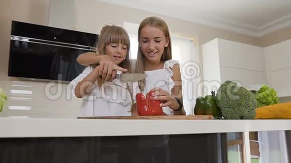 两个穿着白色连衣裙的十几岁女孩在厨房做饭女孩们切红辣椒做沙拉姐姐教的是视频的预览图