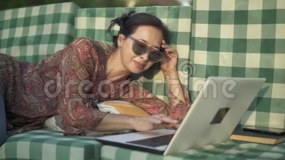 微笑的亚洲女人在外面打手提电脑视频的预览图